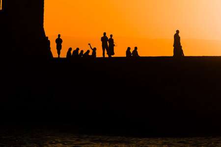 Tourists in silhouette taking photos and selfies in front of a beautiful summer sunsetの写真素材