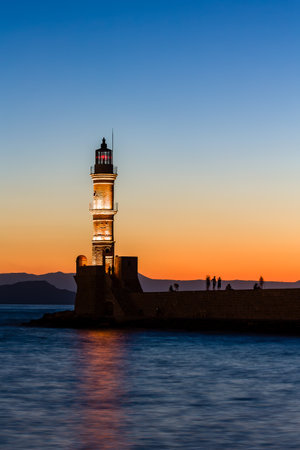Long exposure, blurred image of an old lighthouse at sunset with watching tourists in silhouetteの写真素材