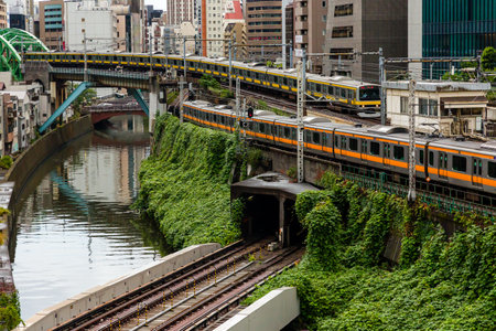TOKYO, JAPAN - AUGUST 09 2023: Trains passing a busy intersection and tunnel over the Kanda River at...