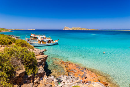 CRETE, GREECE - JULY 12 2023: Large boats full of tourists exploring the clear waters and hot, dry coastline in Kolokitha, near Elounda, Creteのeditorial素材