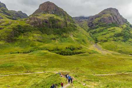 GLENCOE, SCOTLAND - AUGUST 16 2023 - Hikers in the green, dramatic valley of Glen Coe under a moody grey skyのeditorial素材
