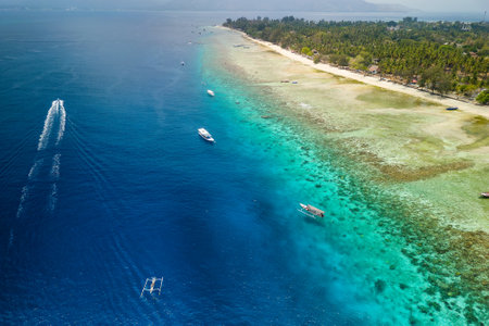 Tourist boats moored on the edge of a fringing coral reef off the coast of a tropical island during a low tideの写真素材