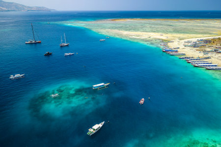 Boats on a beach and coral reef off a tiny tropical island in Indonesia (Gili Air)の写真素材