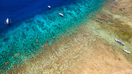 Tourist boats moored on the edge of a fringing coral reef off the coast of a tropical island during a low tideの写真素材