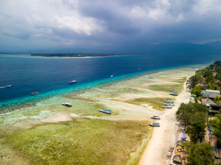 Tourist boats moored on the edge of a fringing coral reef off the coast of a tropical island during a low tideの写真素材