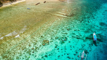 Tourist boats over a tropical coral reef at low tide on the coast of a small tropical (Gili Air, Indonesia)の写真素材