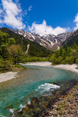 Clear, fast flowing mountain river in a forested valley in front of snowy peaksの写真素材
