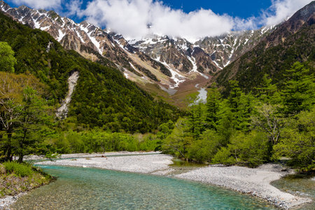Snow covered mountain peaks with a green forest and fast flowing river belowの写真素材