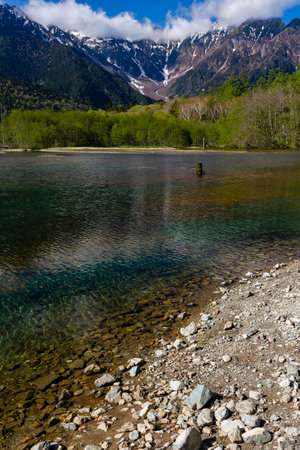 Shallow lake in front of forest and towering snow covered peaks (Hotaka Range, Kamikochi, Japan)の写真素材