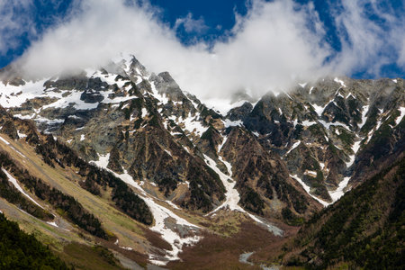 Clouds over the top of tall, jagged, snow covered mountain peaks