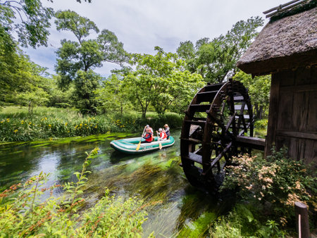 AZUMINO CITY, JAPAN - MAY 28 2023: Tourists on a small boat moving past an old, traditional waterwheel on a small river in Nagano,Japanのeditorial素材