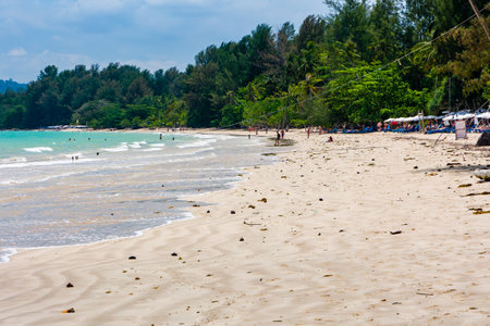 KHAO LAK, THAILAND - APRIL 04 2024: Tourists walking along a sandy, tropical beach surrounded by palm trees in Khao Lak, Thailandのeditorial素材