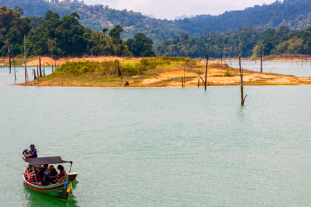 KHAO SOK, THAILAND - APRIL 02 2024:- Wooden longtail boats on the banks of a jungle lake surrounded by lush rainforest and towering limestone cliffsのeditorial素材