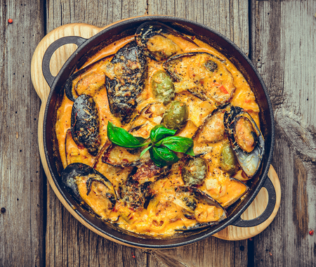 mussels with cheese sauce, in a frying pan, wooden backgroundの写真素材
