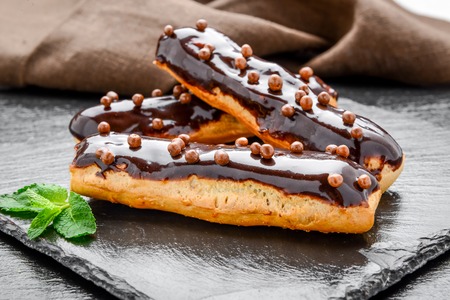 Traditional French dessert. Eclair with chocolate icing and raspberries. Dark backgroundの写真素材