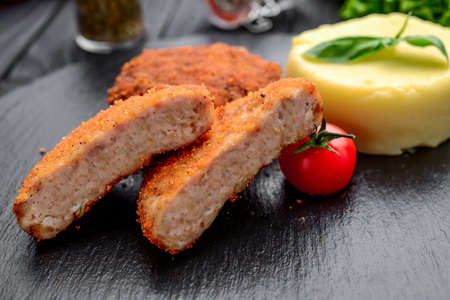Cutlet with boiled potatoes on a black plateの写真素材