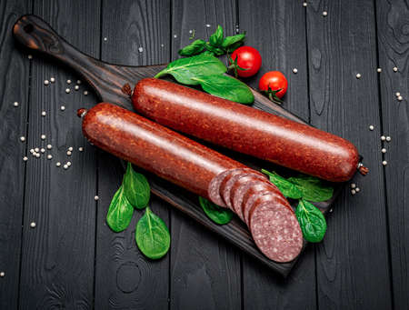 Smoked sausage on a dark background with spices, garlic and basil. salami.の写真素材