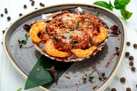 Shrimps baked in scallop shell with tomato sauce and vegetables. Serving food in a restaurant. Photo for the menuの写真素材