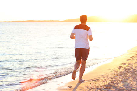 the guy runs along the seashore against the sunsetの写真素材