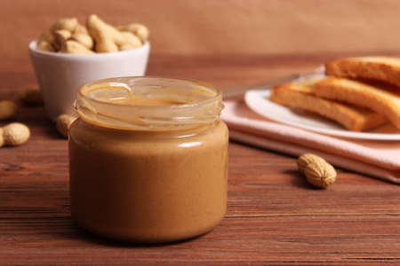 creamy peanut butter and peanuts beans on wooden background top view