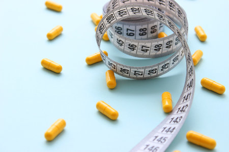 Measuring tape and diet pills on a colored background close-up.