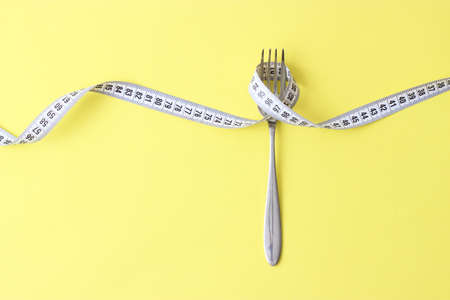 Measuring tape and fork on a colored background top view close-up.