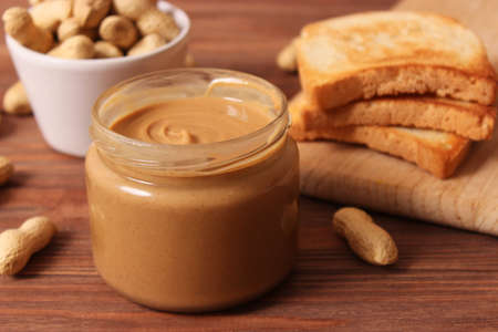 creamy peanut butter and peanuts beans on wooden background top view
