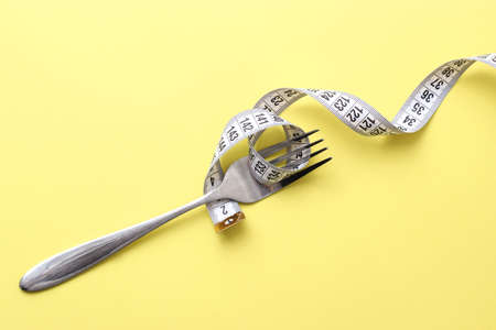 Measuring tape and fork on a colored background top view close-up.