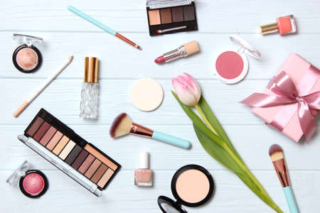 makeup products and beautiful spring flowers on wooden background. Top view.