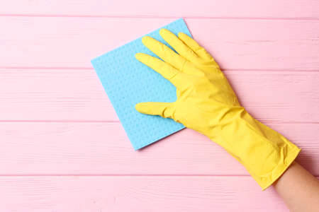 female hand in cleaning glove and rag on colored background