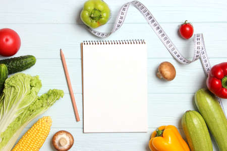 Fresh vegetables, measuring tape and paper notepad on wooden table.の写真素材