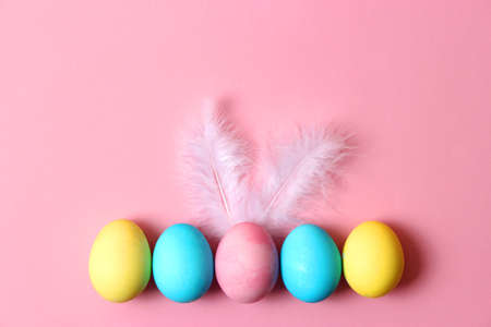 Easter composition of painted eggs and feathers on a colored background.