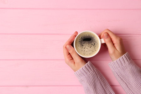 Cup of coffee with frothy in female hands on wooden table. Top view.の写真素材