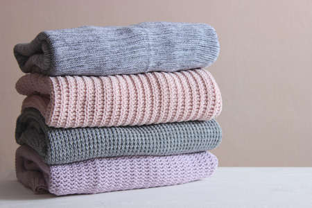 Warm knitted sweaters folded in a stack on a light background close-up.