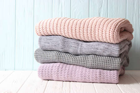 Warm knitted sweaters folded in a stack on a light background close-up.