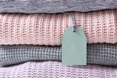 Warm knitted sweaters folded in a stack on a light background close-up.