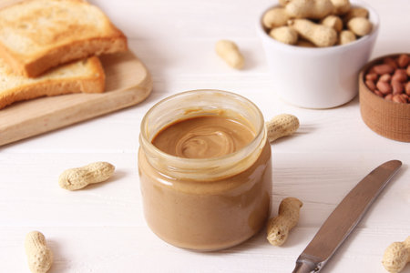 creamy peanut butter and peanuts beans on wooden background top view