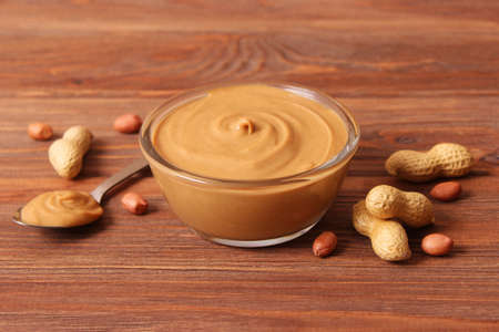 creamy peanut butter and peanuts beans on wooden background top view