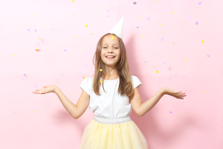 Portrait of a little girl in a festive cap on a colored background and confetti.の写真素材