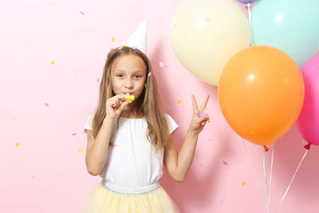Portrait of cute girl in a festive cap and with balloons on colored background.