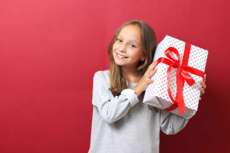 cute cheerful girl in a Christmas hat on a colored background holding a giftの写真素材