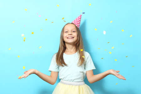 Portrait of a little girl in a festive cap on a colored background and confetti.の写真素材