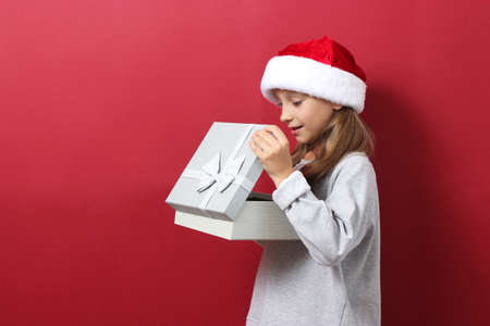 cute cheerful girl in a Christmas hat on a colored background holding a giftの写真素材
