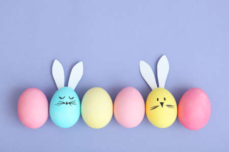 Easter eggs with cute faces and ears on a colored background.