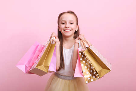 Beautiful smiling little girl with bags for shopping on a colored background.の写真素材