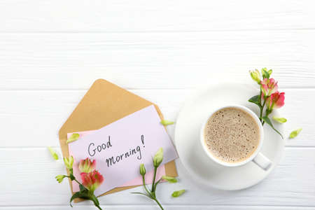 A cup of coffee, a bouquet of flowers and a card with the words good morning.の写真素材