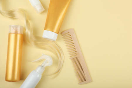 A lock of blonde hair, hair care products and a comb on a colored backgroundの写真素材