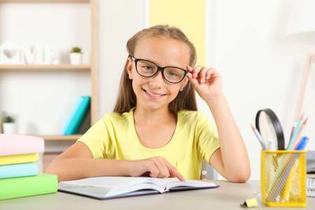 Little girl with glasses reading a book at homeの写真素材