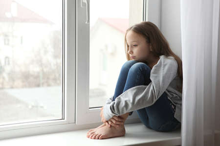 Lonely sad girl at home. saddened alarmed child alone at home.の写真素材
