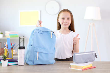 Cute cheerful schoolgirl puts stationery in a backpack.の写真素材